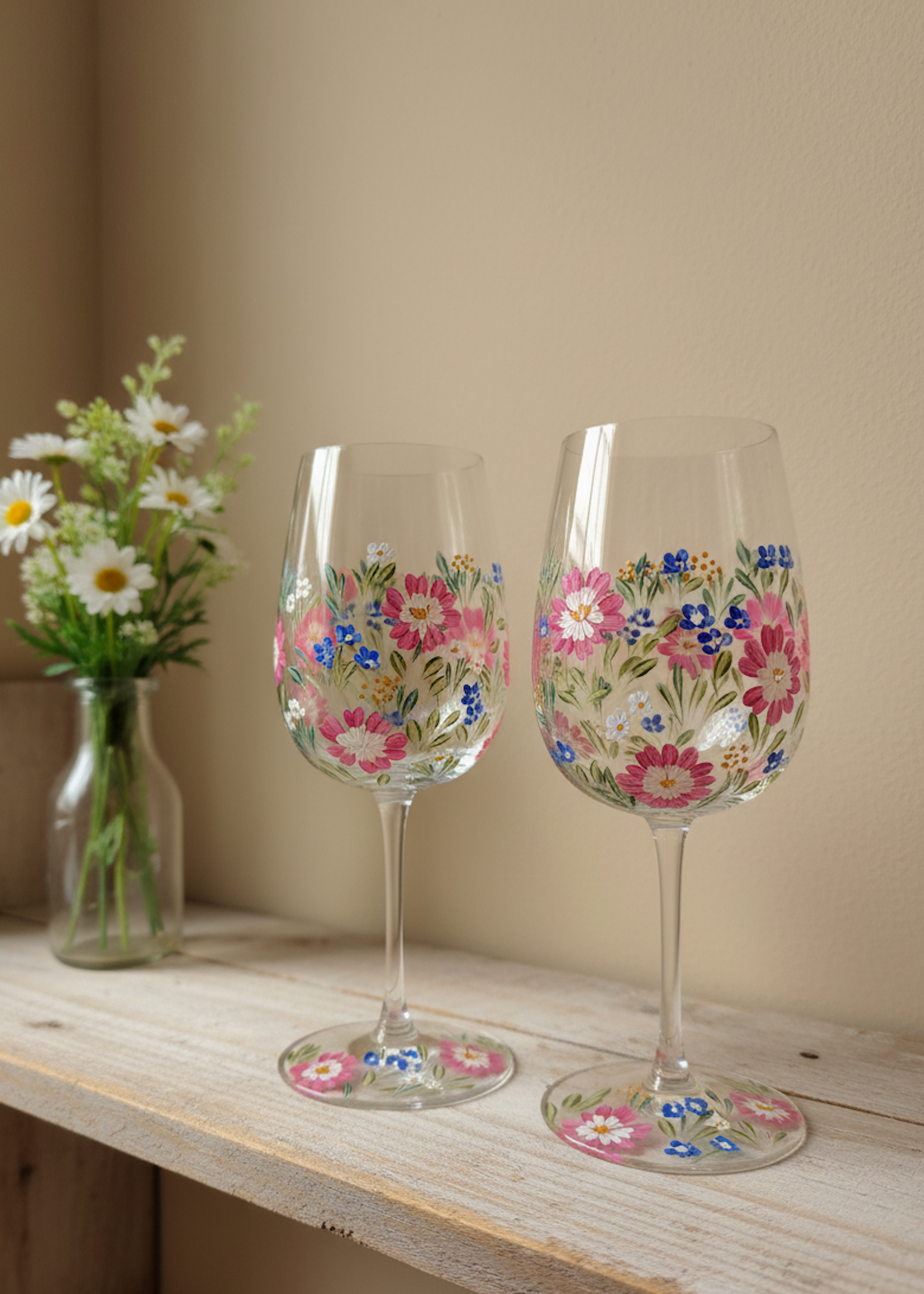 Two floral-patterned wine glasses on a wooden surface with a vase of flowers in the background.